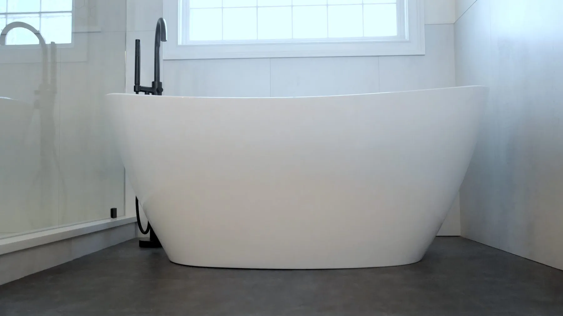 Freestanding tub on a concrete-look porcelain floor with large-format tile walls
