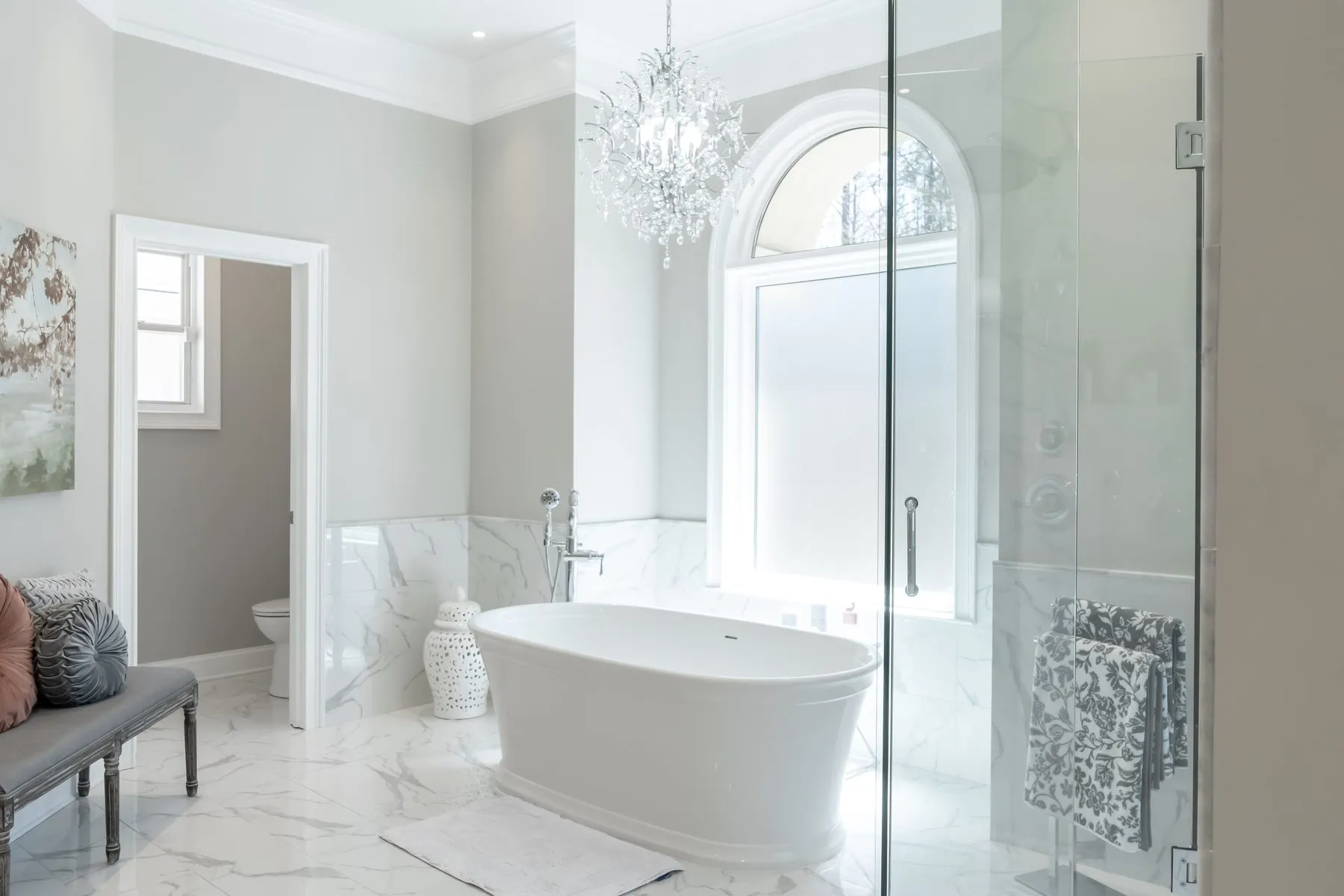 Marble master bathroom with a freestanding tub, chandelier and book-matched porcelain wall tile
