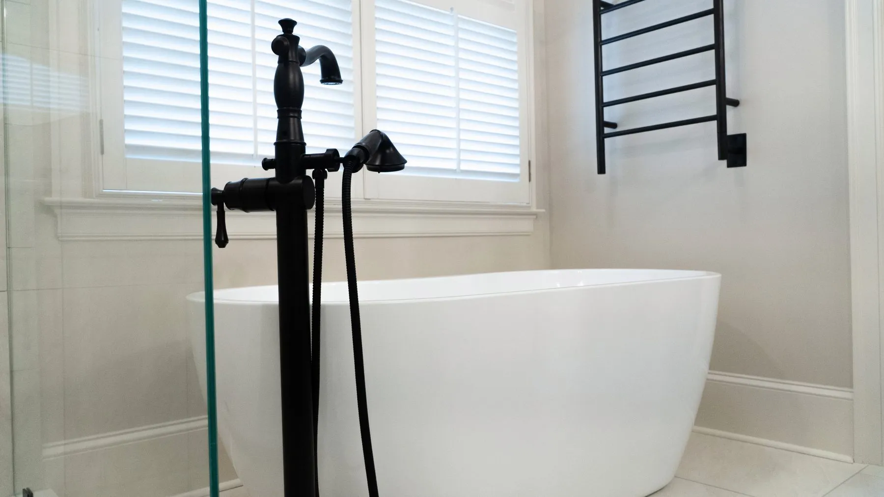 Master bathroom with a freestanding tub beneath a shuttered window and a wall-mounted towel warmer