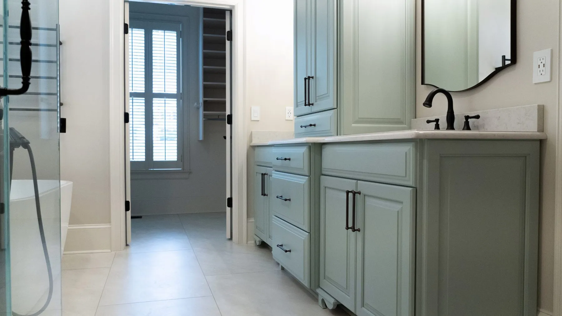 Long vanity run in sage cabinetry with large-format porcelain floor tile running through to the hallway