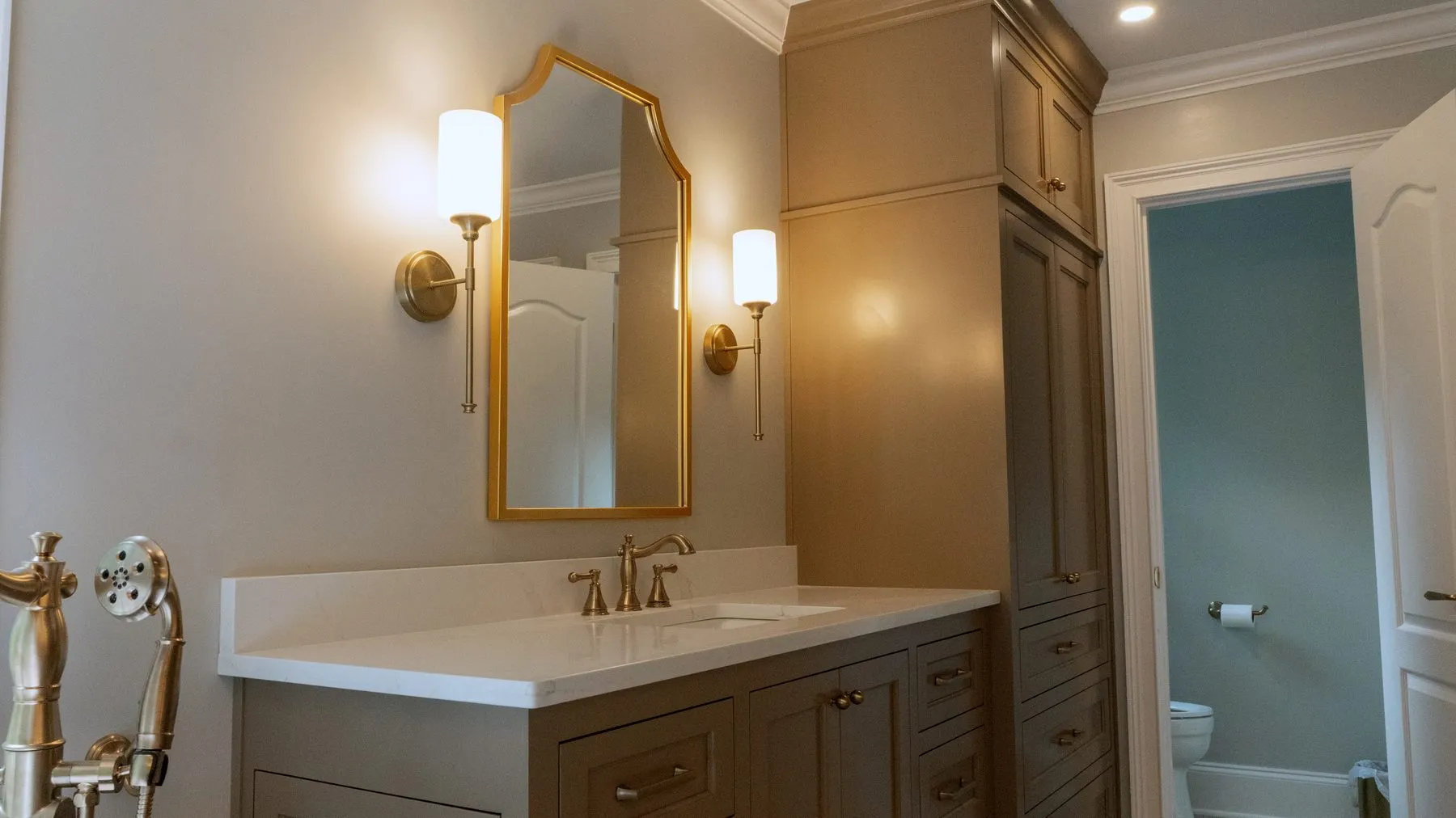 Bathroom vanity in taupe cabinetry with quartz top, brass fittings and a gold-framed mirror