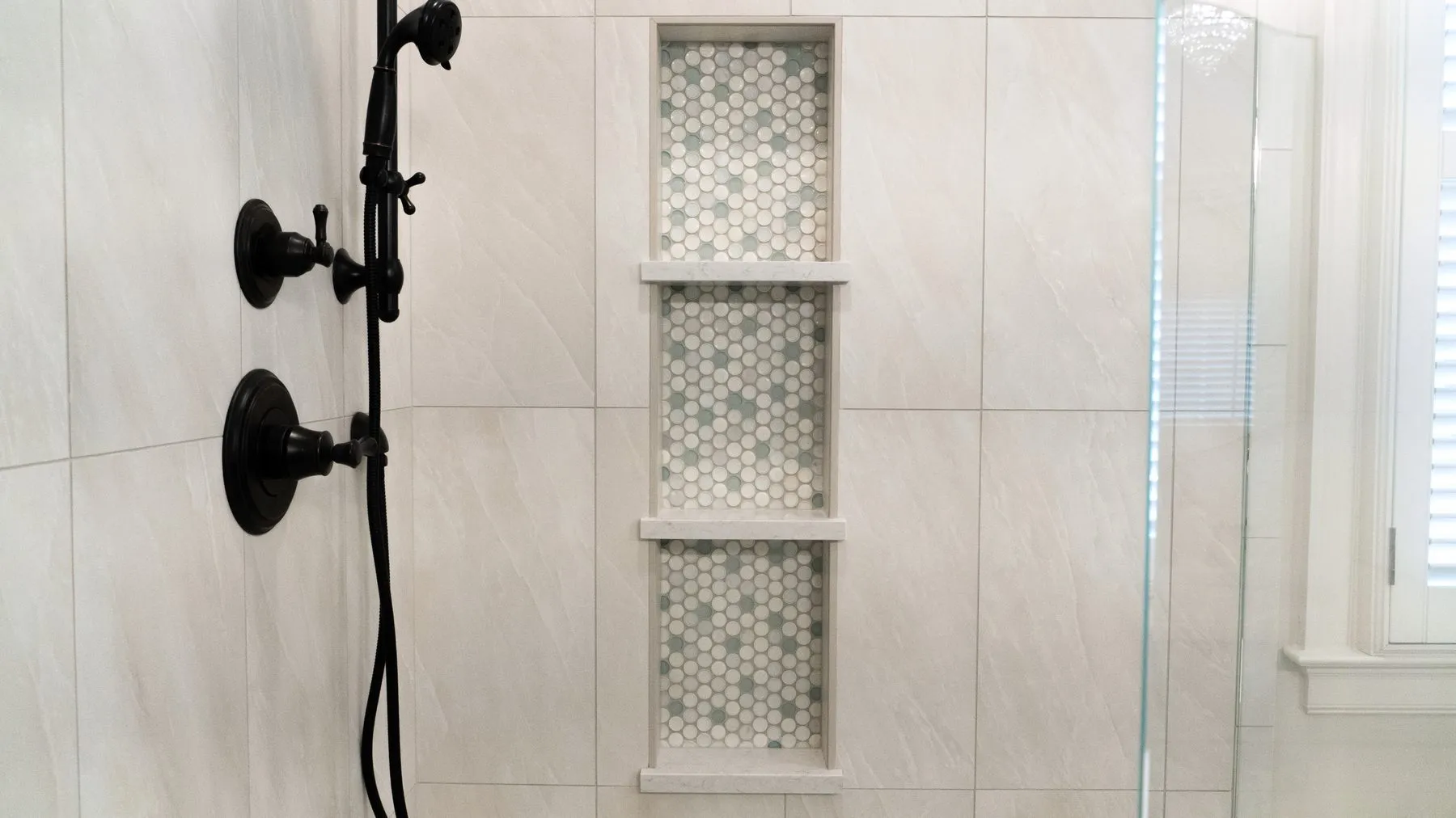 Recessed shower niche divided into three shelves and lined with pale mosaic tile