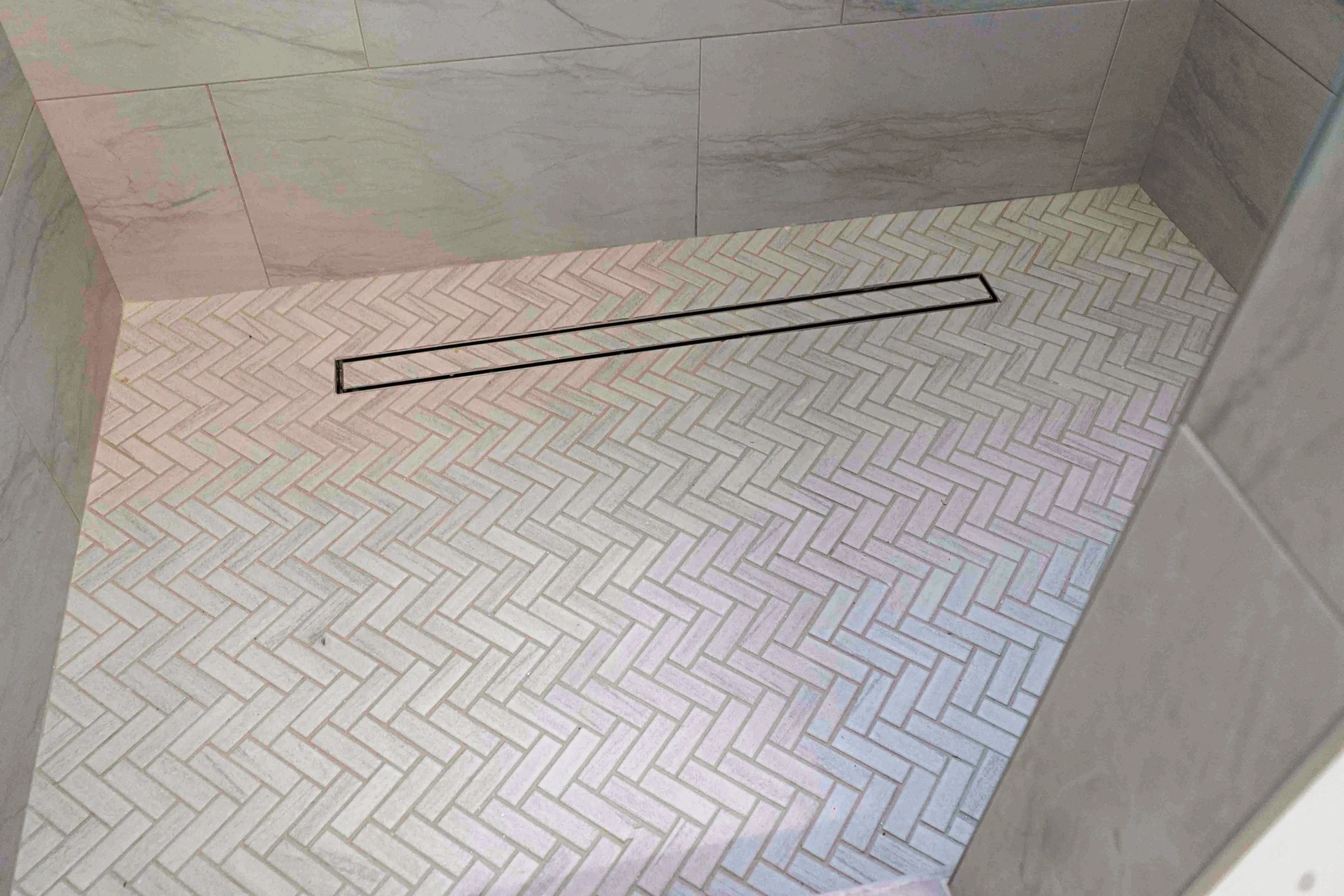 Herringbone marble floor tile with a linear drain in a walk-in shower