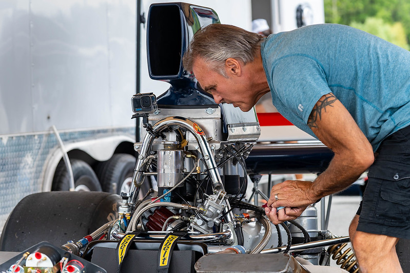 Man closely inspecting the engine of a drag racing car in a garage area.