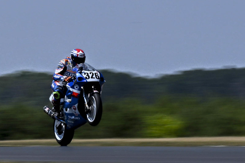 Motorcycle racer in full gear performing a wheelie on a blue Suzuki racing bike numbered 326 on a track.