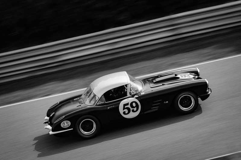 Black and white photo of a vintage race car with number 59 driving on a racetrack.