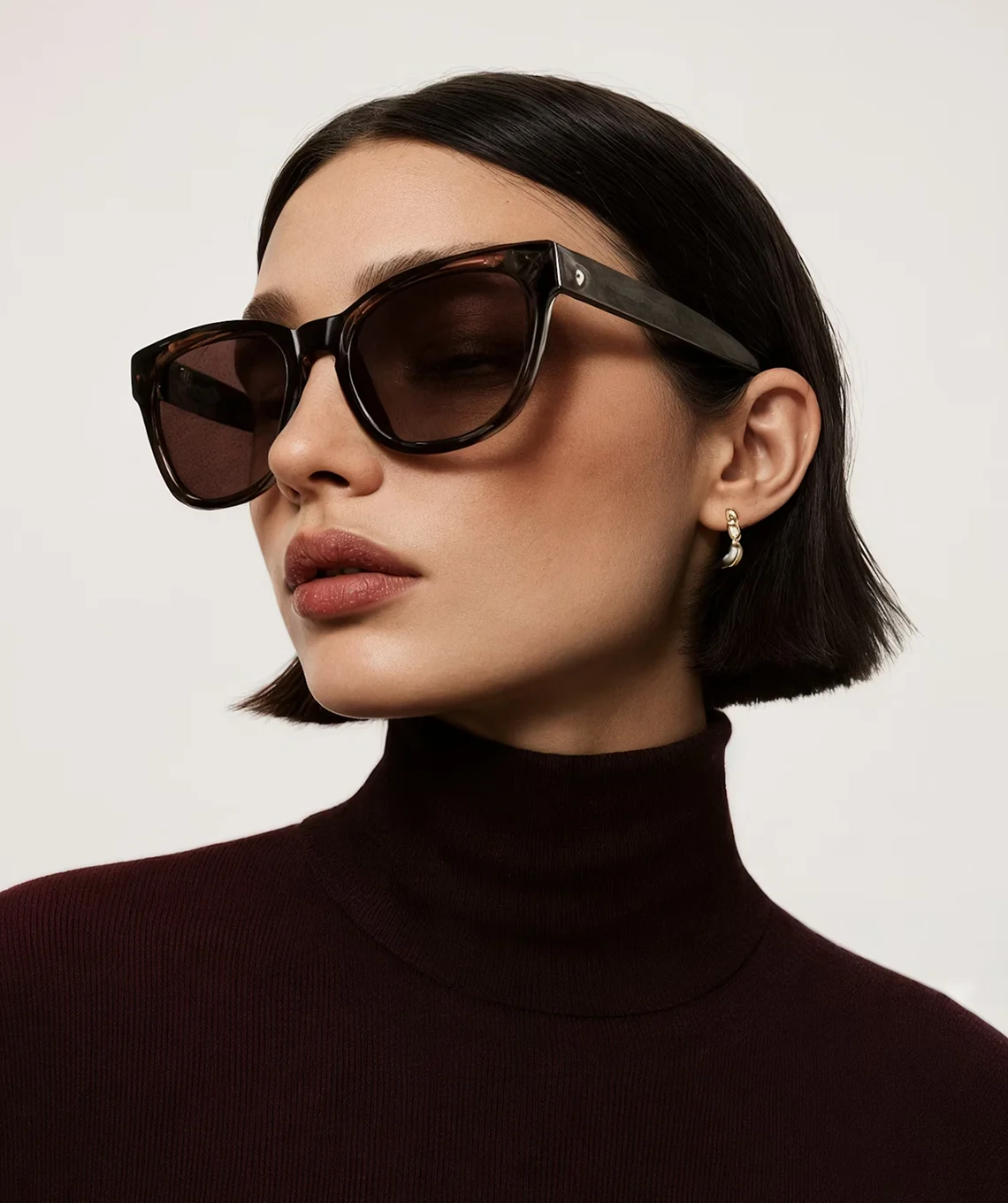 A woman wearing sunglasses and a turtle neck sweater.