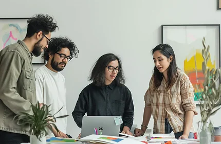 A group of people standing around a table with a laptop.