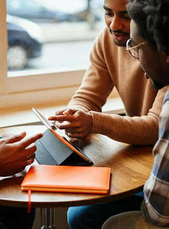 Two men sitting at a table looking at a tablet.