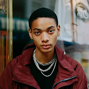 A young man wearing a red jacket and a black shirt.