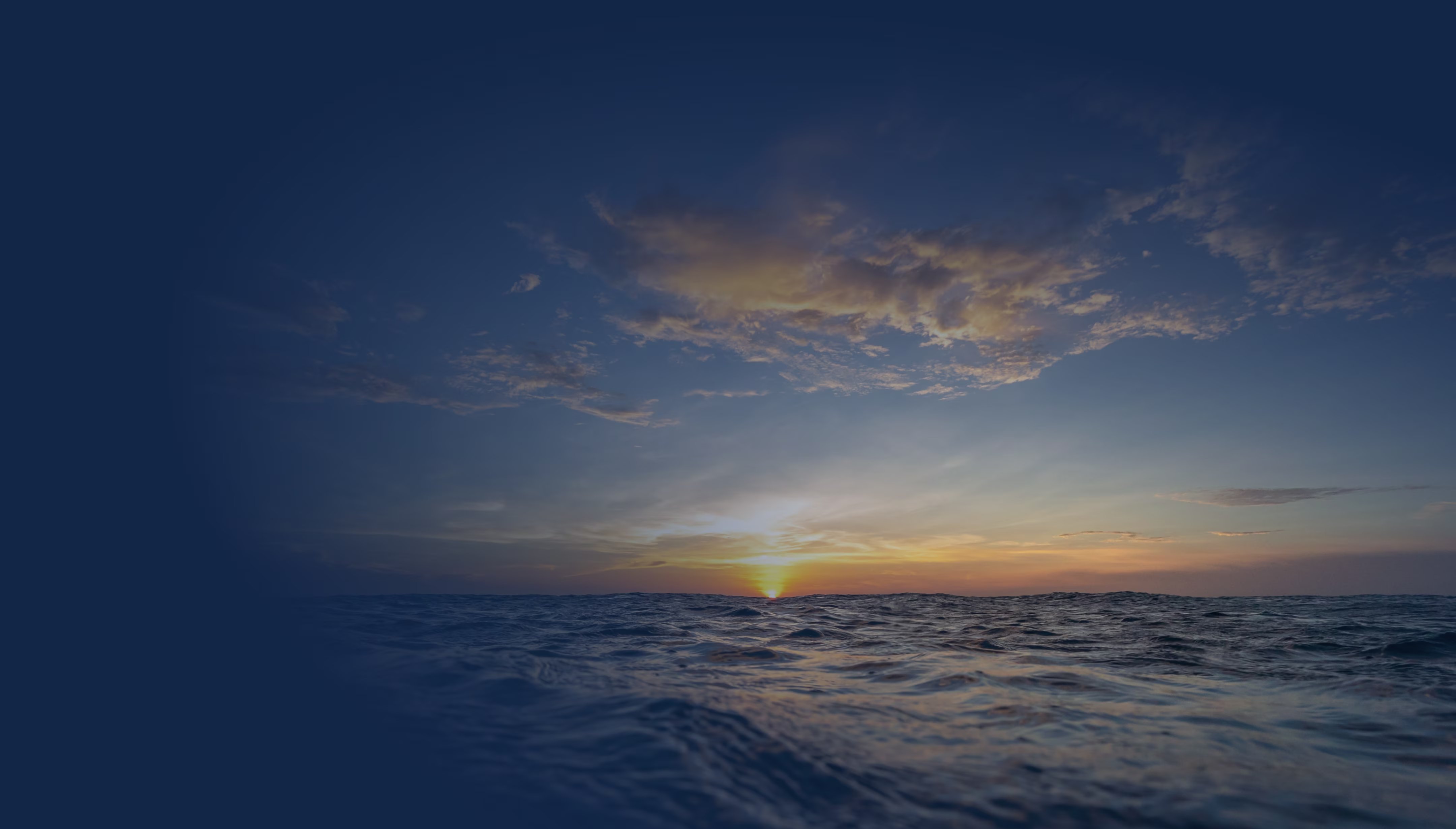 Sunset over a calm ocean with scattered clouds reflecting golden light on the water surface.