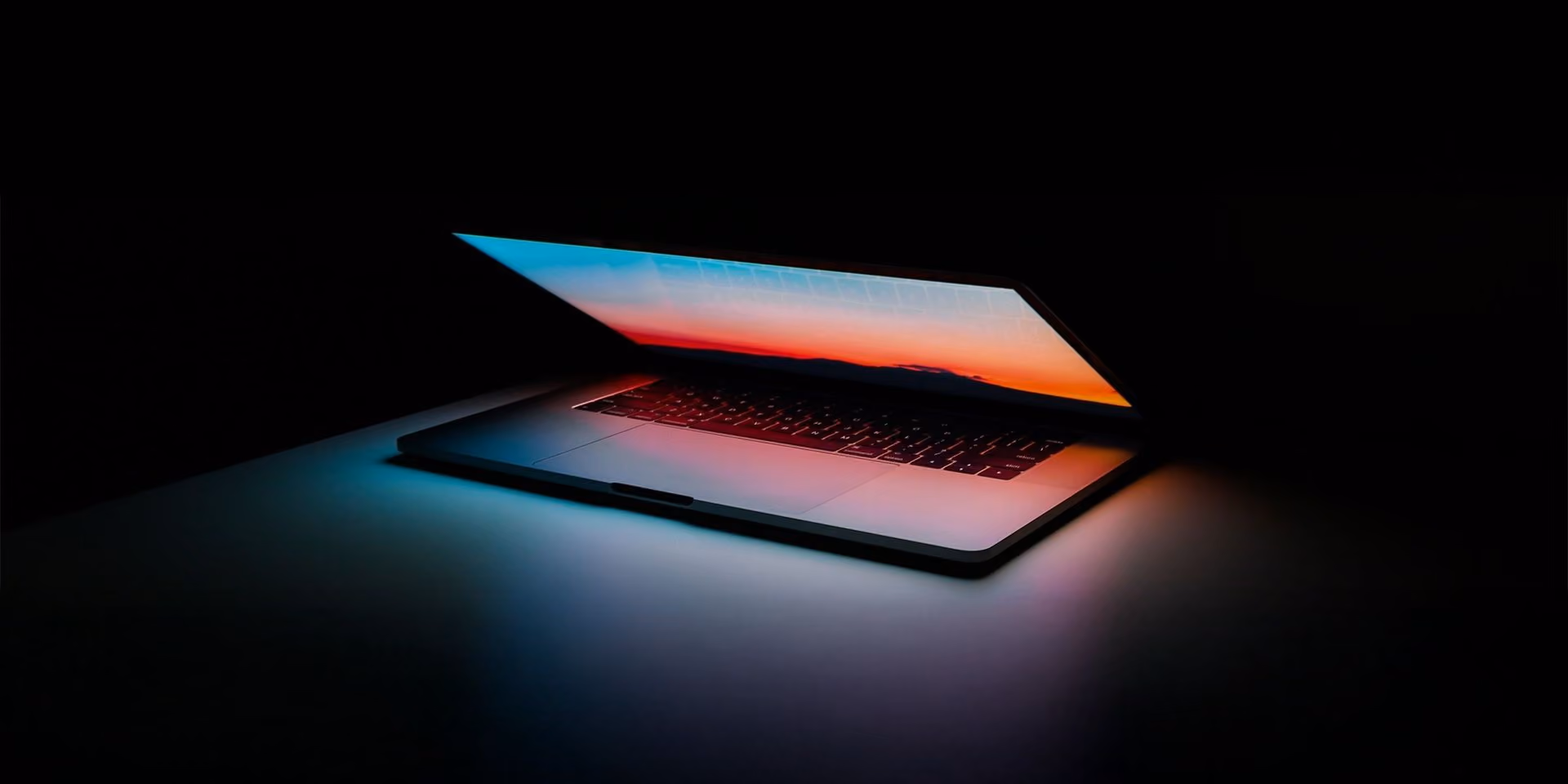 Atvērtas klēpjdatora tastatūras apgaismojums tumsā ar sarkani zilu gaismu.