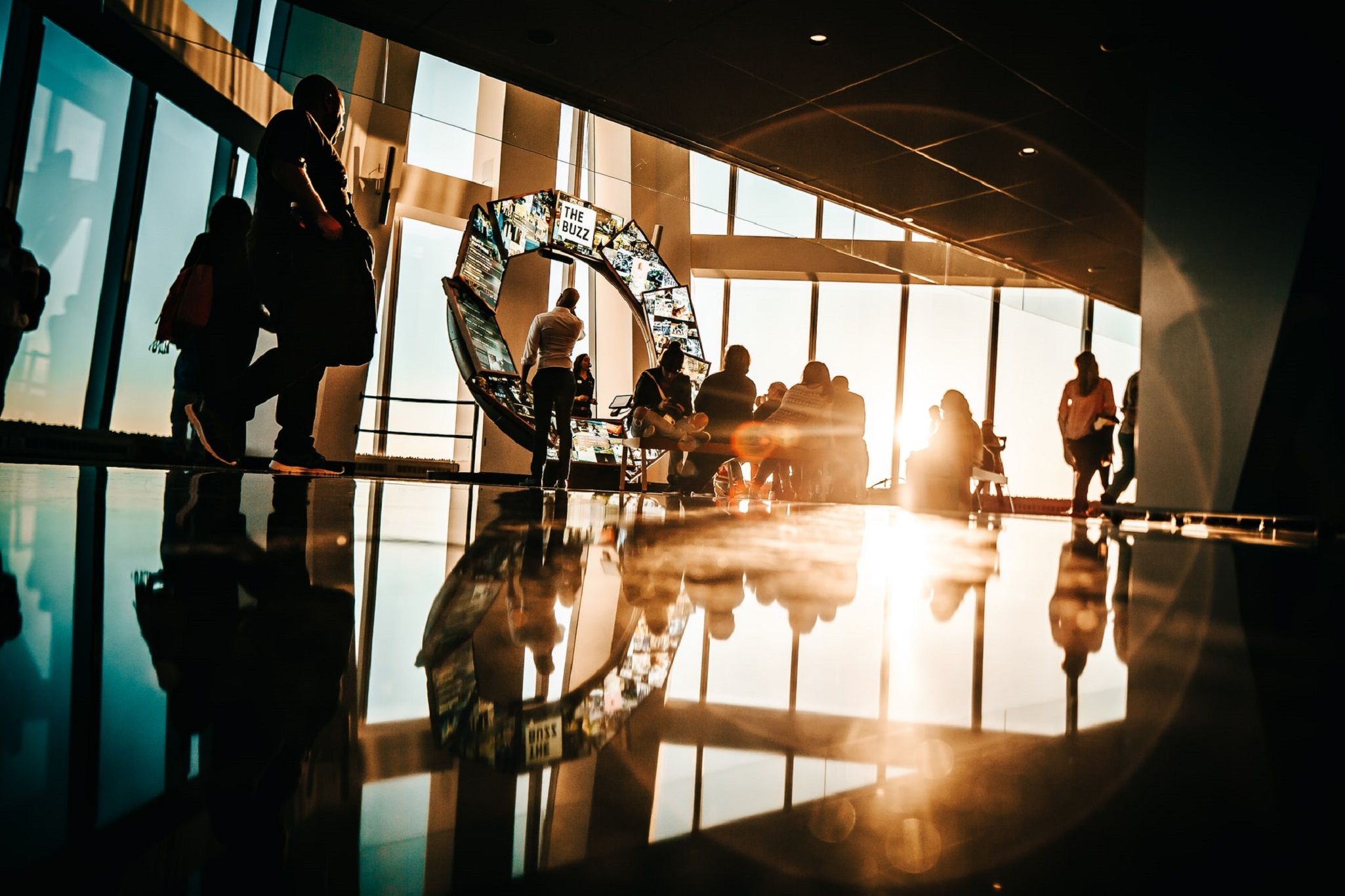 Sunlight streams through windows into a bright, modern office atrium with people and art installations.