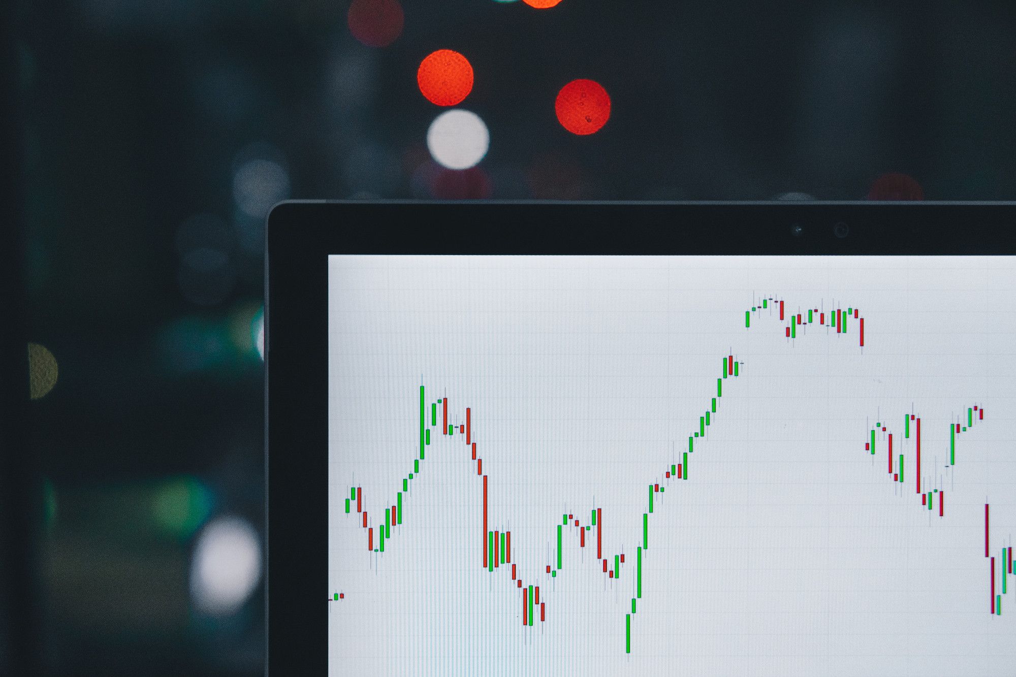 A computer screen showing a financial chart and a price-change curve, with blurred lights in the background.