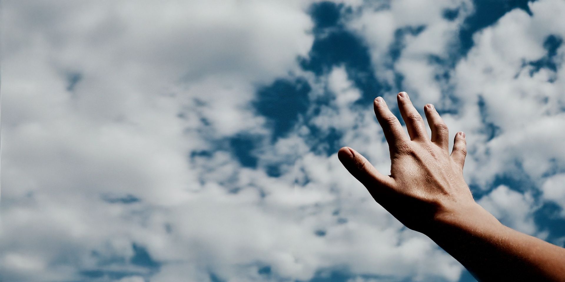 A hand raised against a blue sky with light clouds.