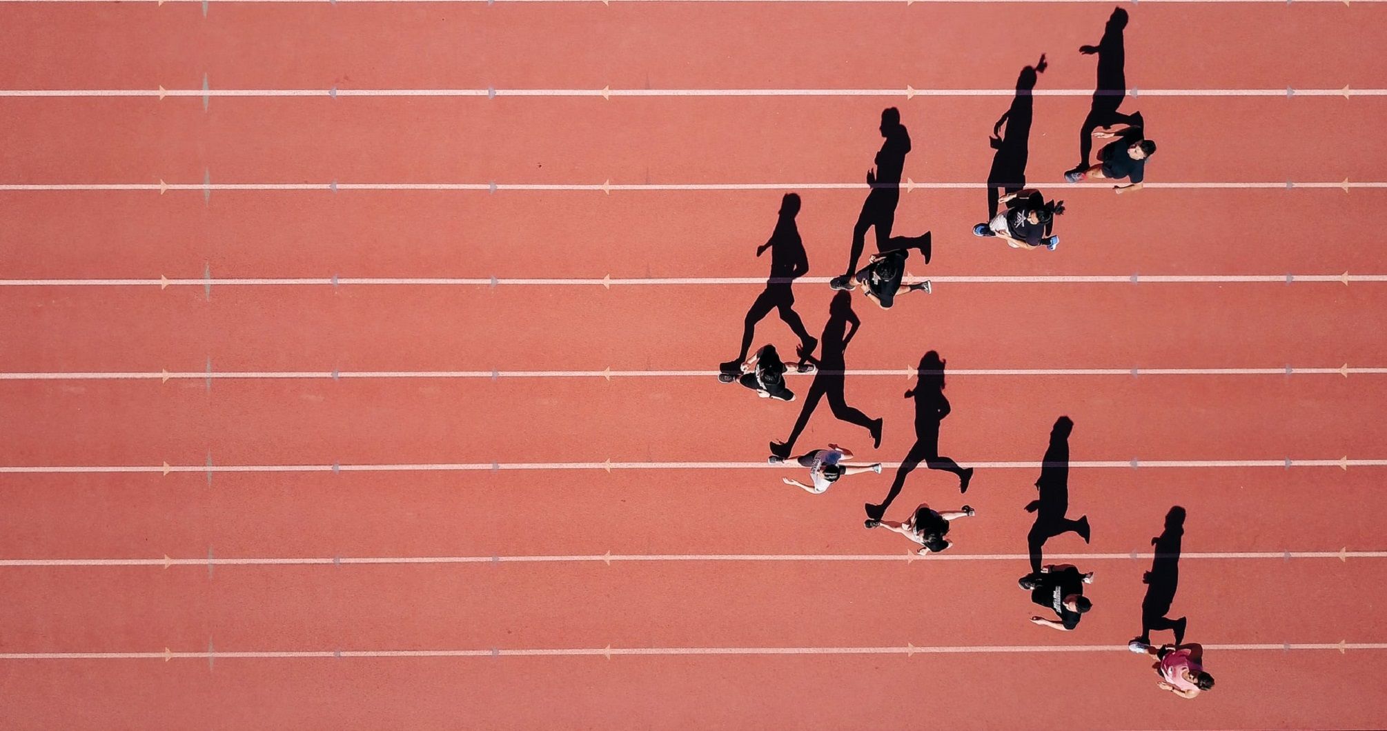 An overhead view of runners on a sports track, their shadows stretching across the lanes.