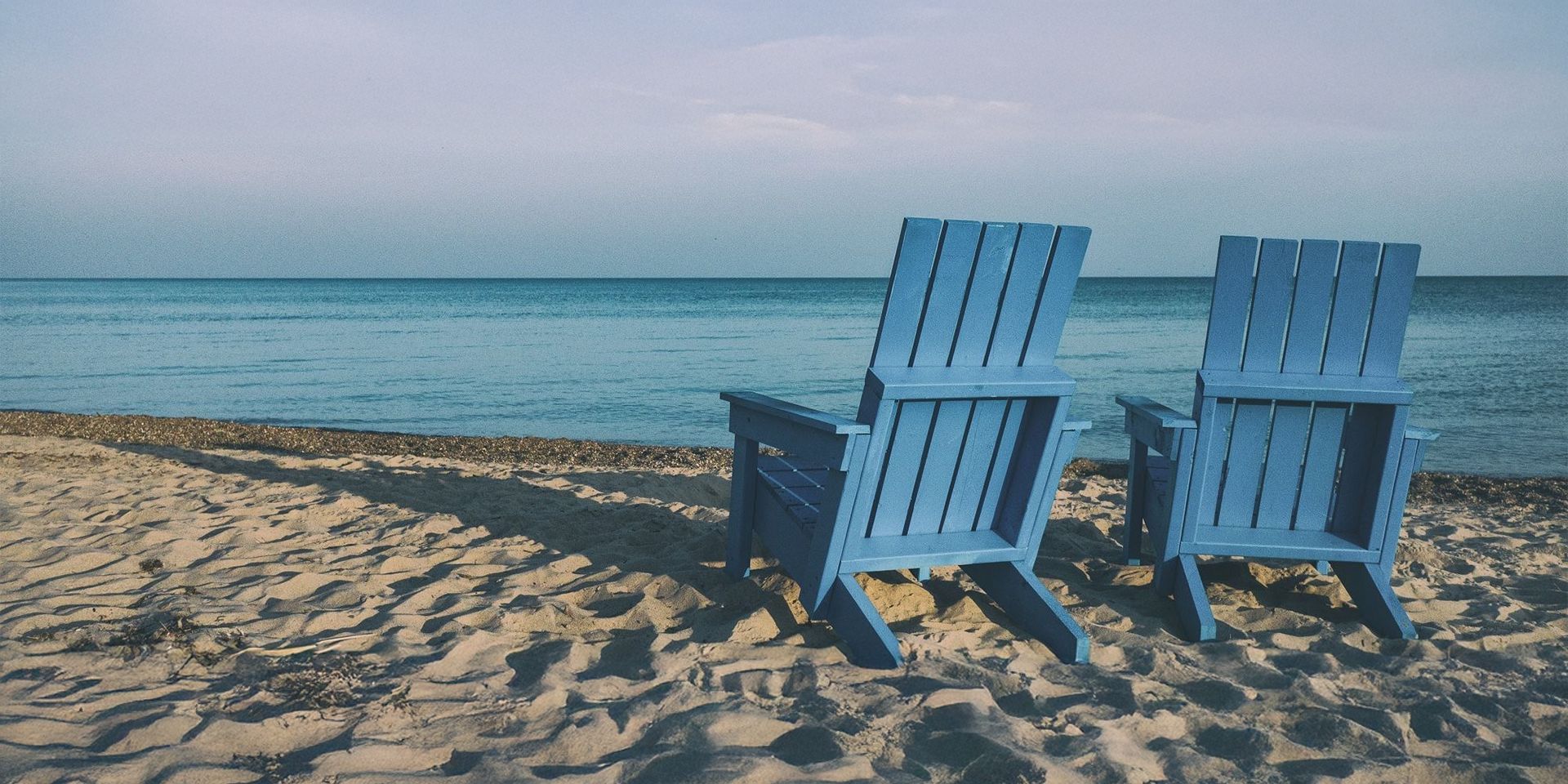 Two wooden beach chairs on a sandy beach with the sea in the background.