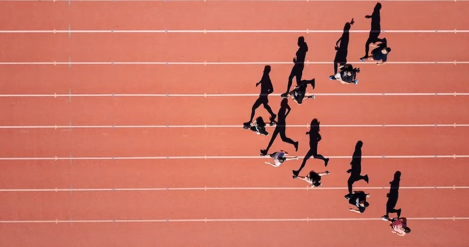 Skats no augšas uz skrējējiem sporta stadionā, viņu ēnas izstiepjas pa skrejceļu.