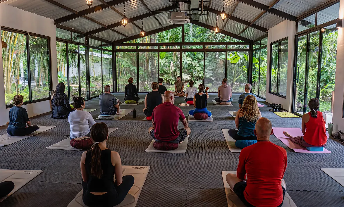 Group meditation session inside a glass wellness pavilion surrounded by nature