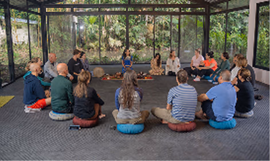 Group meditation circle inside a glass wellness pavilion surrounded by jungle
