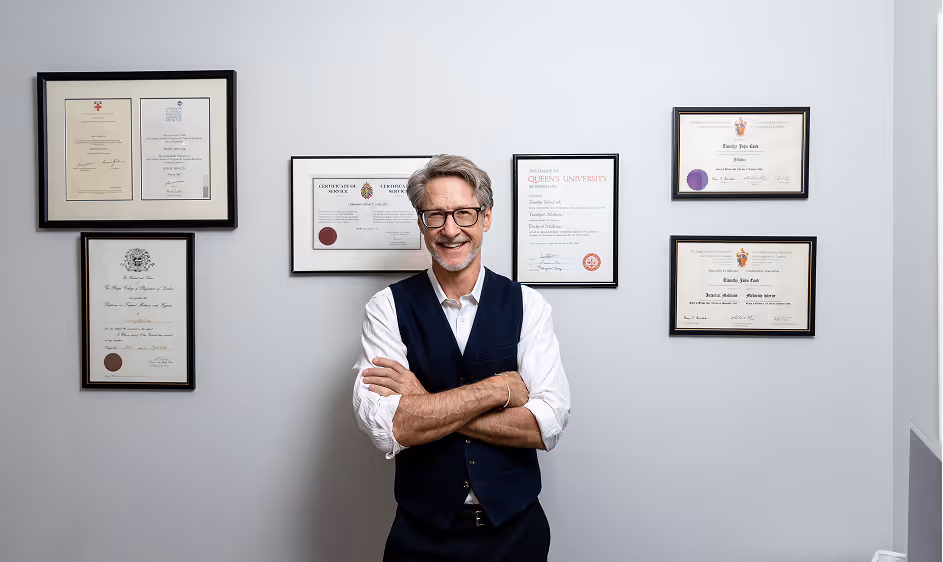 Doctor smiling in front of medical certificates and diplomas on clinic wall