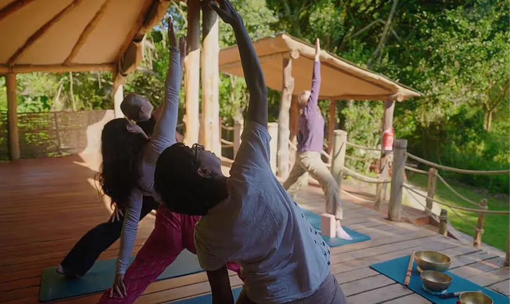 Group yoga session on an open-air wooden deck surrounded by nature