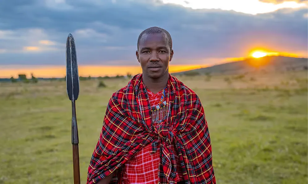 Maasai warrior standing at sunset on the African plains holding a spear