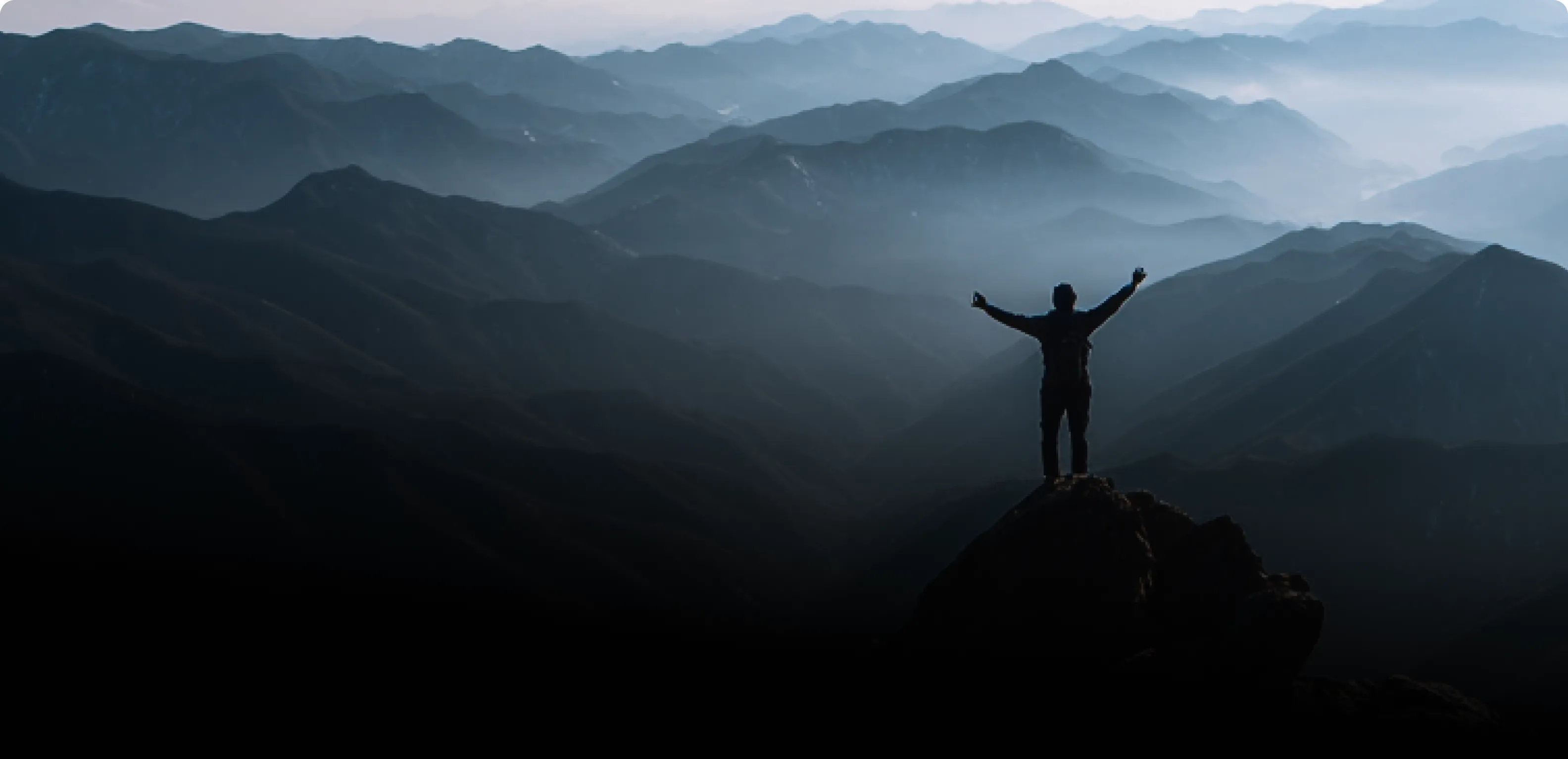 Silhouette of a person standing on a mountain peak with arms raised in triumph
