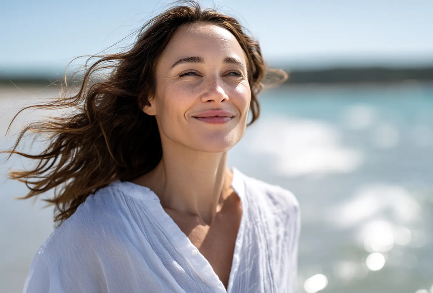Woman with flowing hair smiling peacefully by the ocean