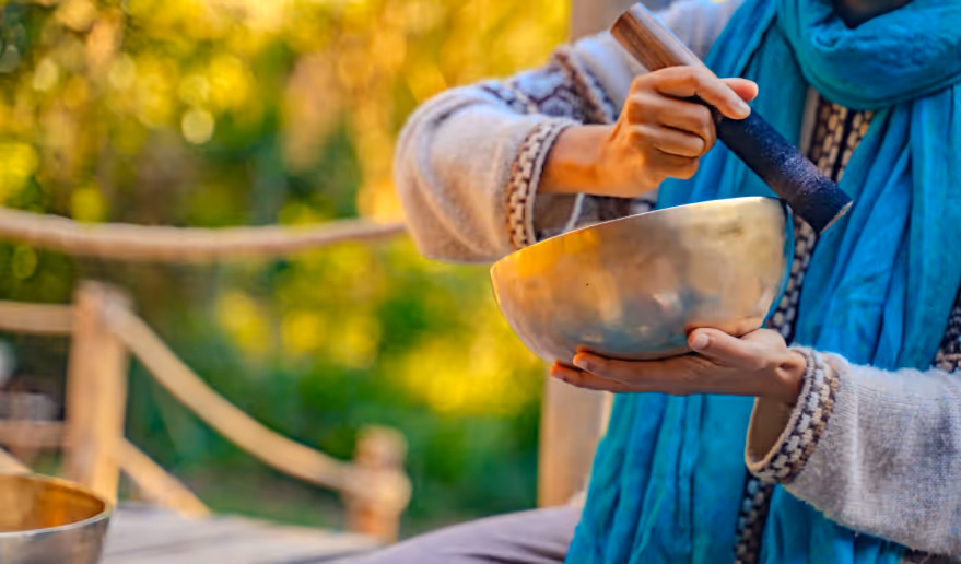 Wellness facilitator playing a Tibetan singing bowl during an outdoor session