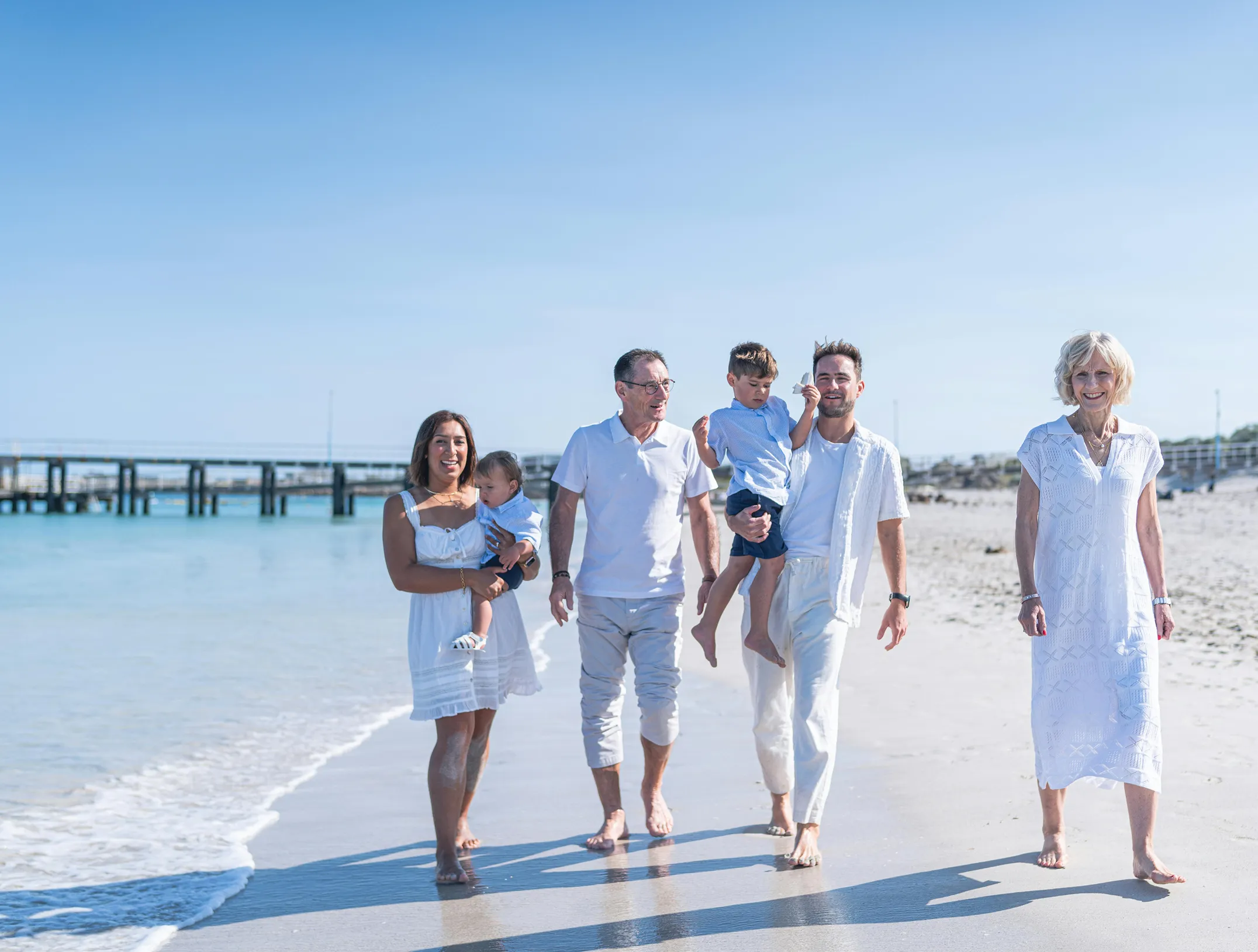 A multi-generational family walking together on the beach at sunset