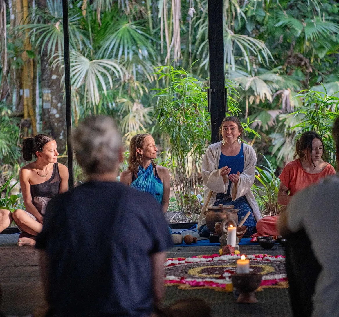 Group of people sitting in a circle during a wellness retreat in a tropical outdoor setting