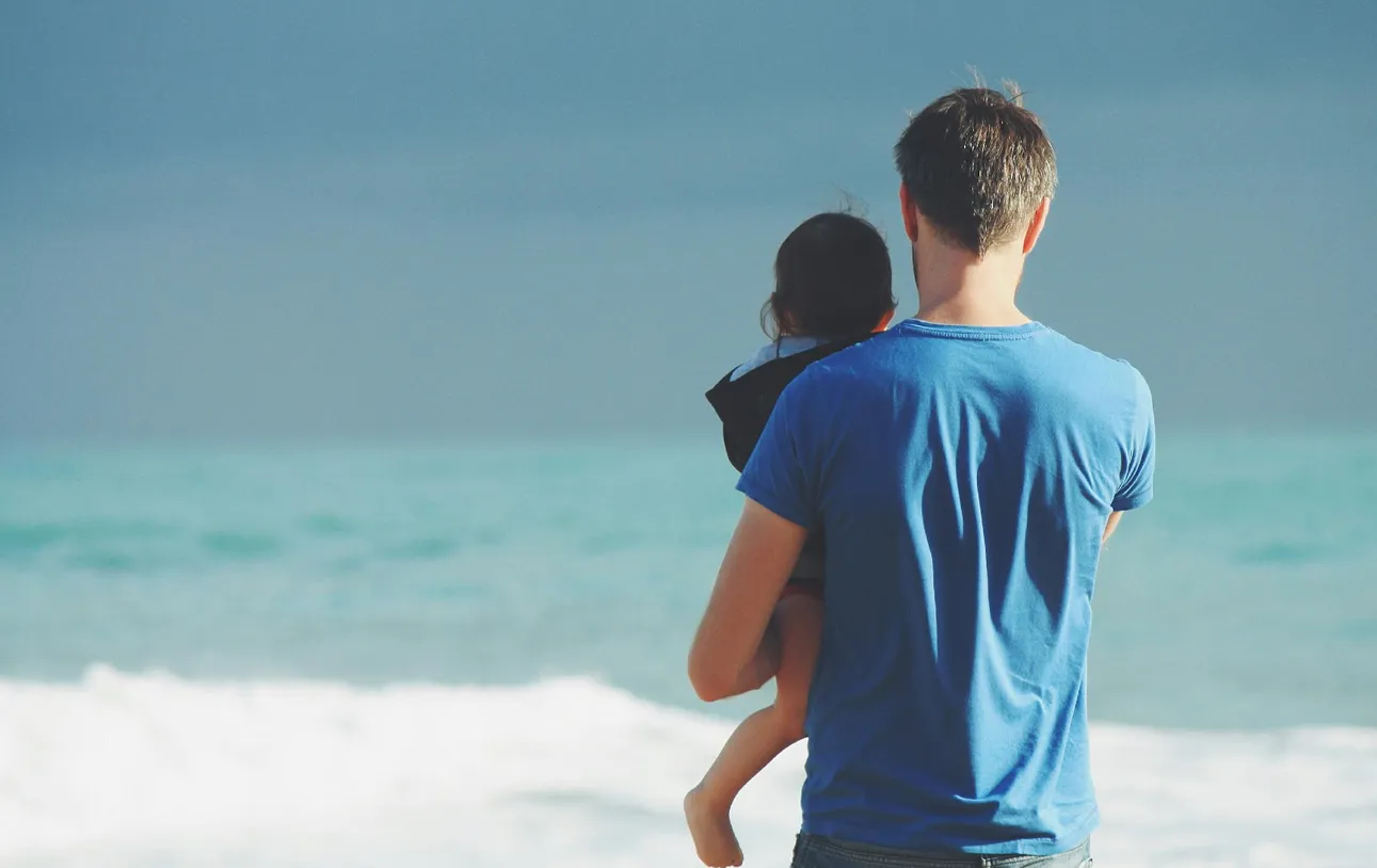Father carrying child on his shoulders walking by the ocean