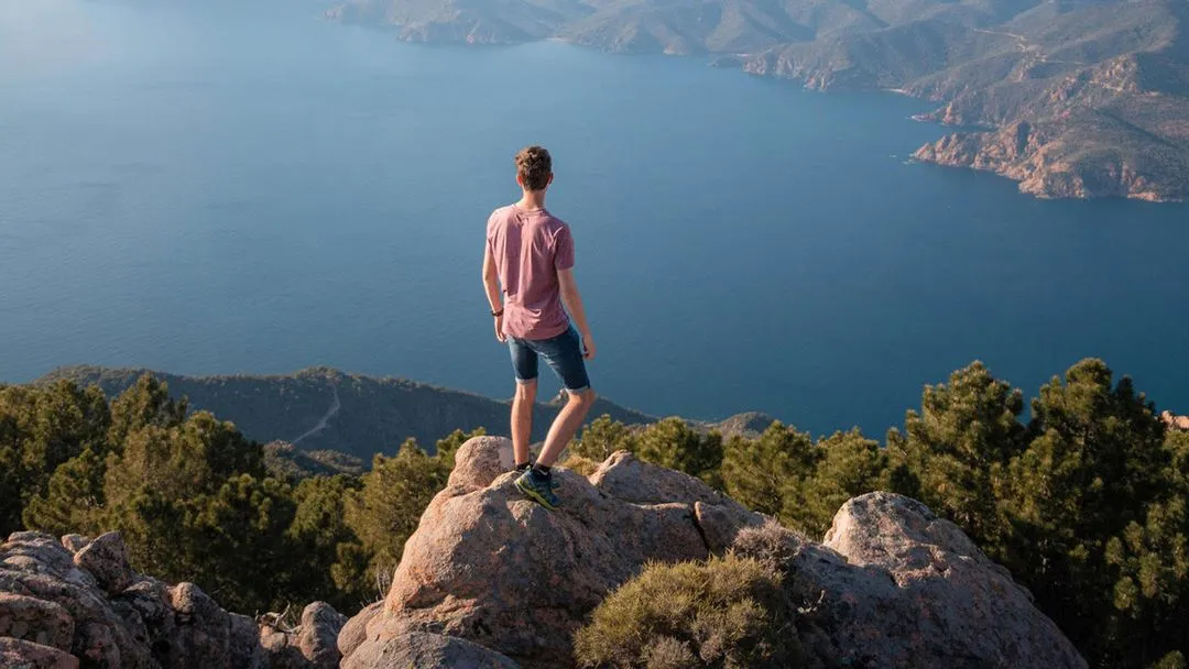 Person standing on a mountain cliff overlooking a lake