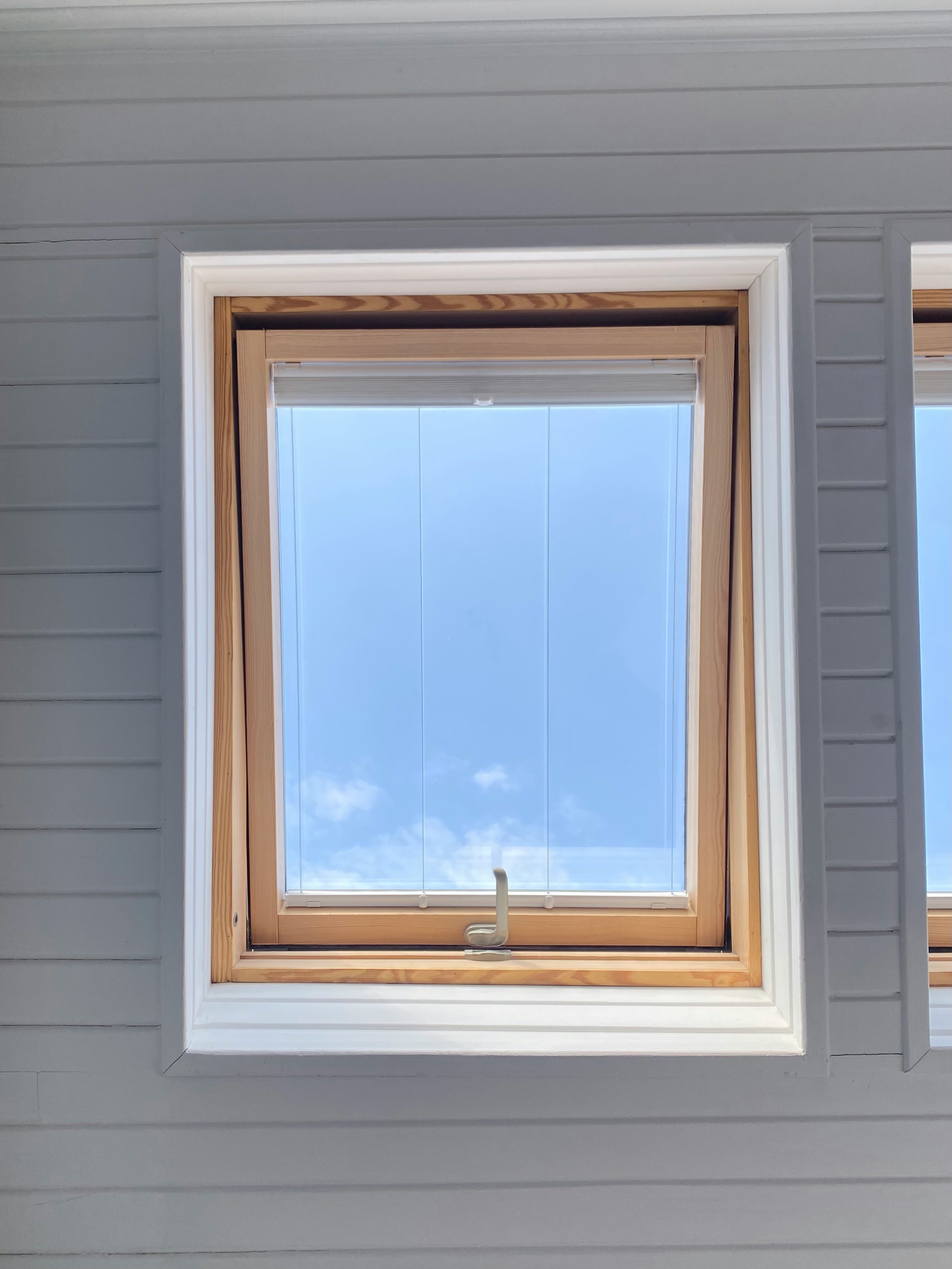 Ett takfönster med träram i ett vitt innertak, med utsikt mot en blå himmel med moln.