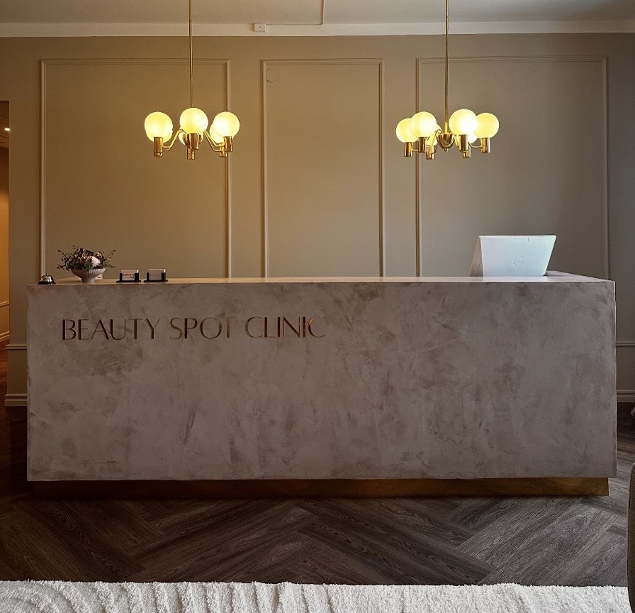 Receptionen på Beauty Spot Clinic med två moderna takkronor och en dator på disken.