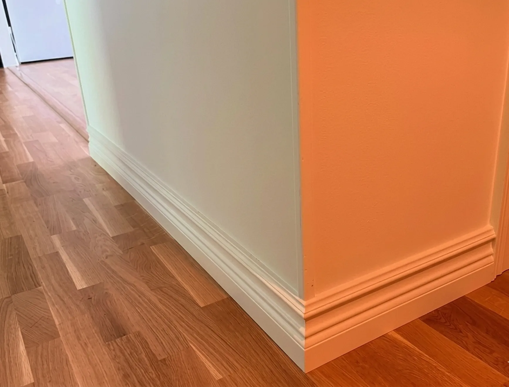 Närbild på en vit hörnlist som möter nylagt golv. 