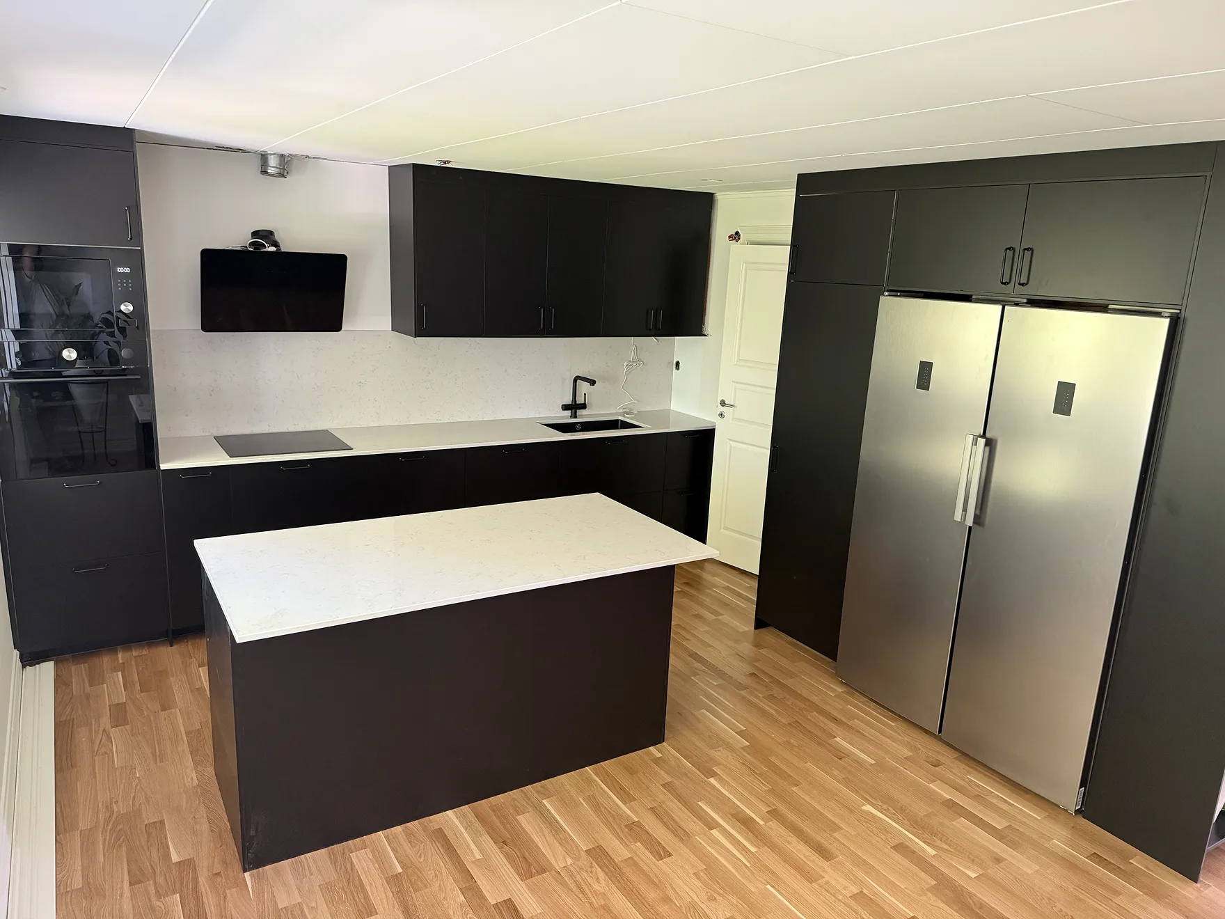 Översikt av köksrenovering med svart köksö och vit bänkskiva, vitvaror i silver och svart köksinredning. 