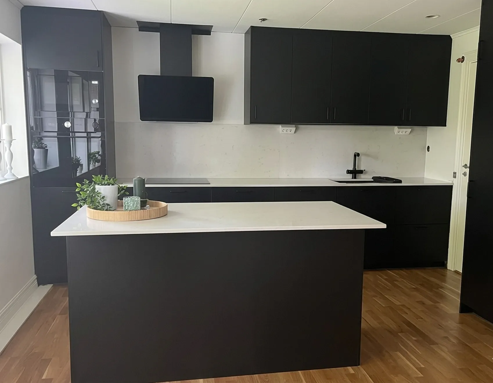 Närbild på svart köksö och vit bänkskiva med svart köksinredning i bakgrunden. 