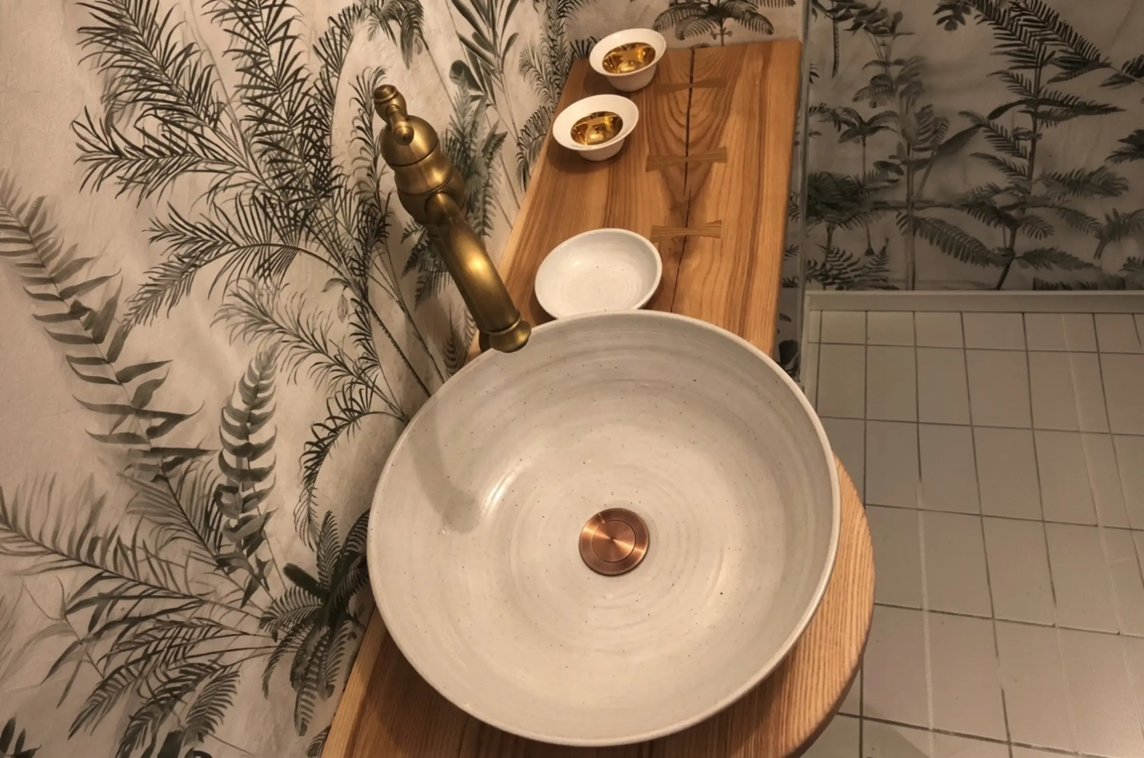 Platsbyggd bänkskiva i massiv ask med mässingskran och handgjord keramiktvättskål – badrumsrenovering i Gävle av JMH Bygg