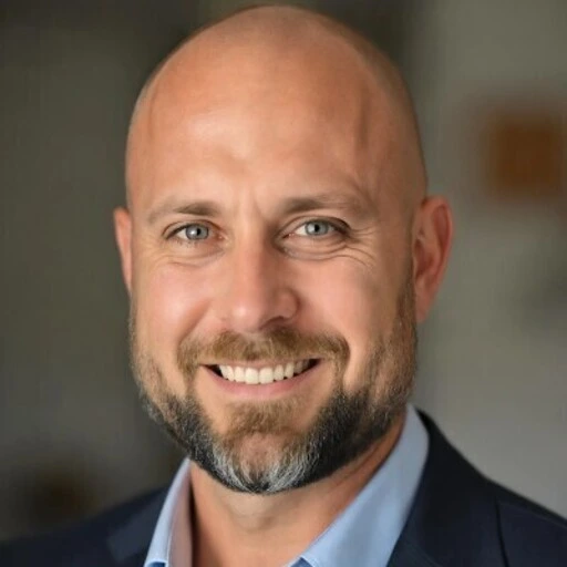 Smiling bald man with blue eyes and beard wearing a dark suit and light blue shirt.