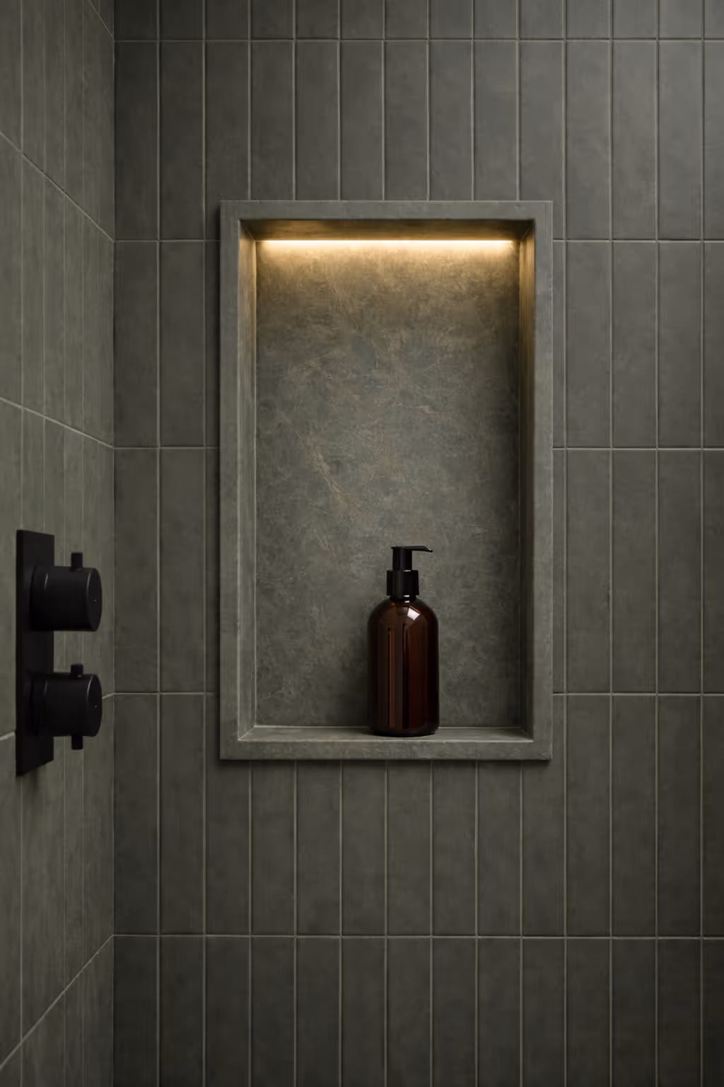 Backlit shower niche with dark brown pump bottle mounted in vertical gray tile wall.