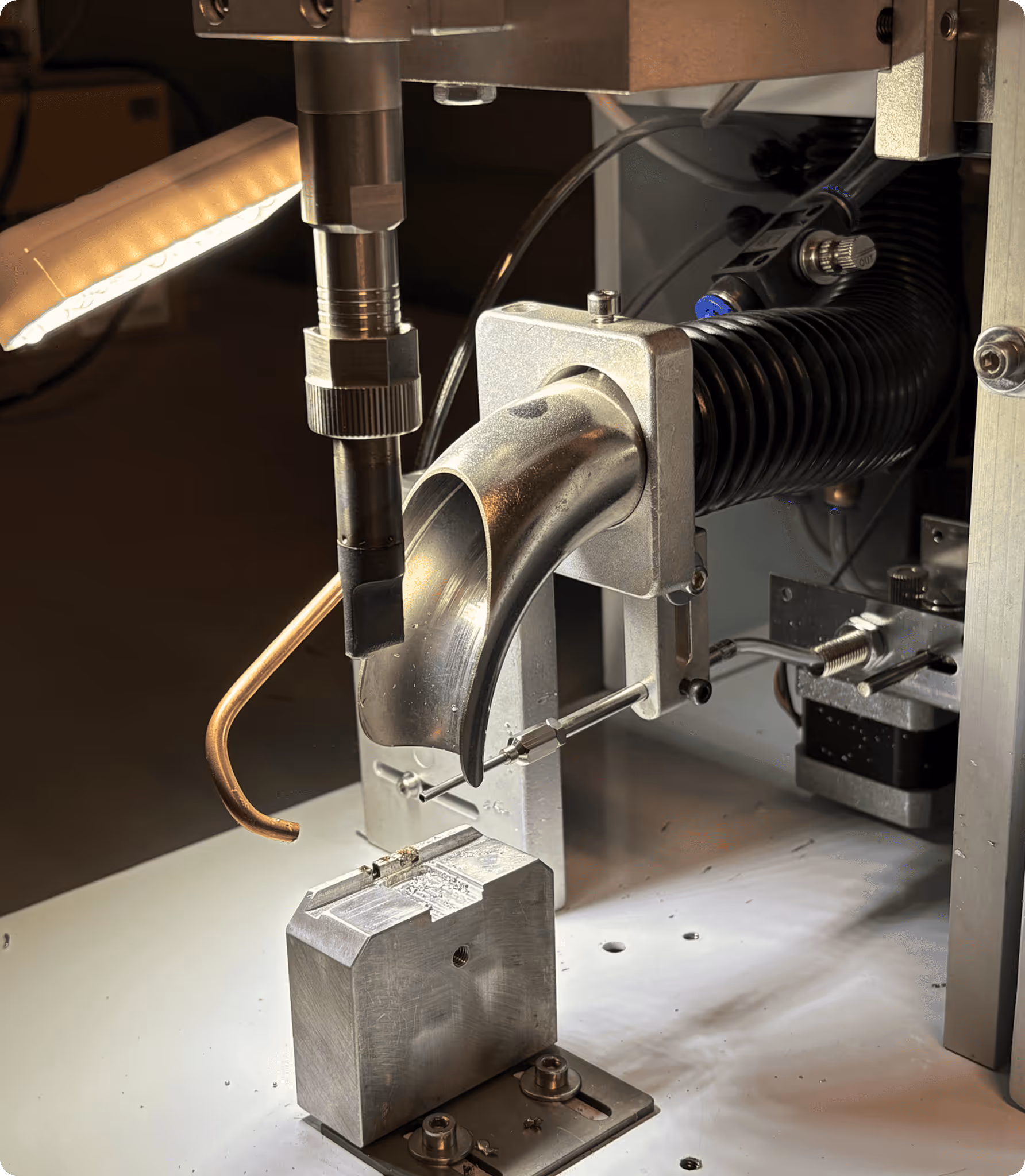 Close-up of a metal machine part with a curved chute and mechanical components on a white base.