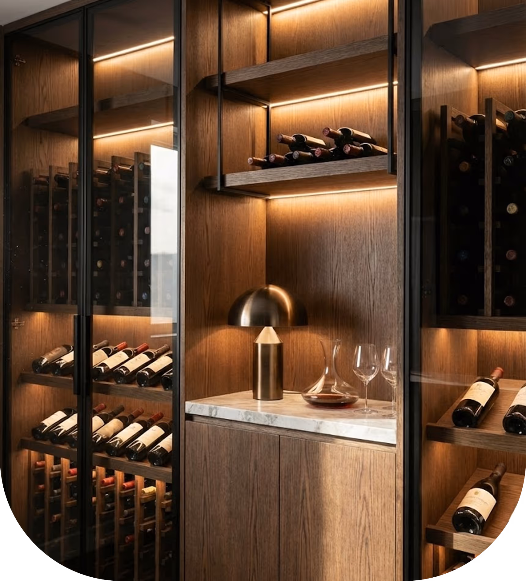 Modern wine cellar with wood cabinets, glass doors, wine bottles, a golden lamp, and glassware on marble.