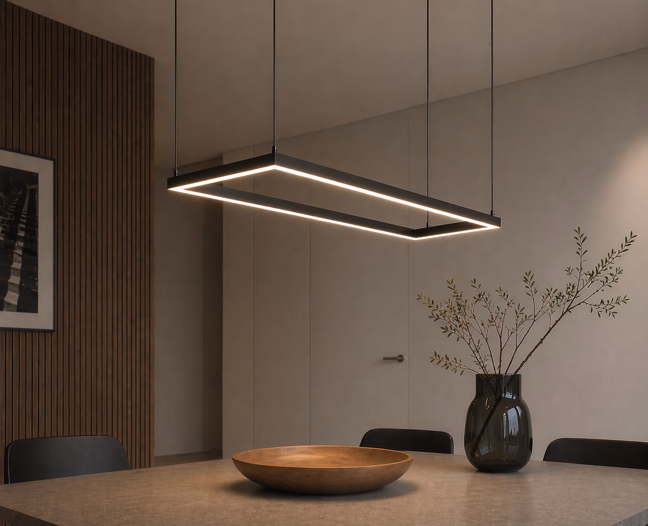 Modern dining room with a rectangular hanging LED light, wooden bowl, and vase with branches.