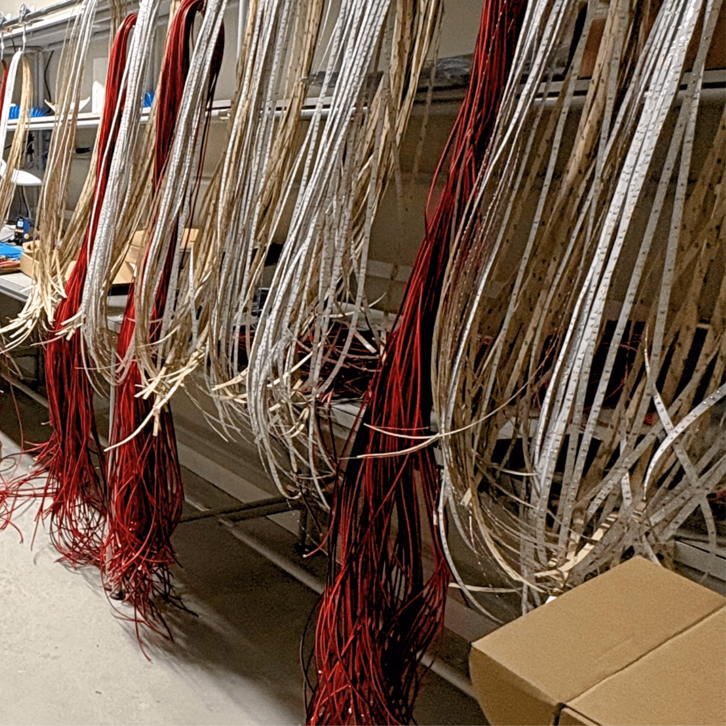 Bundles of red and white wires hanging in a factory workspace with boxes and shelves.
