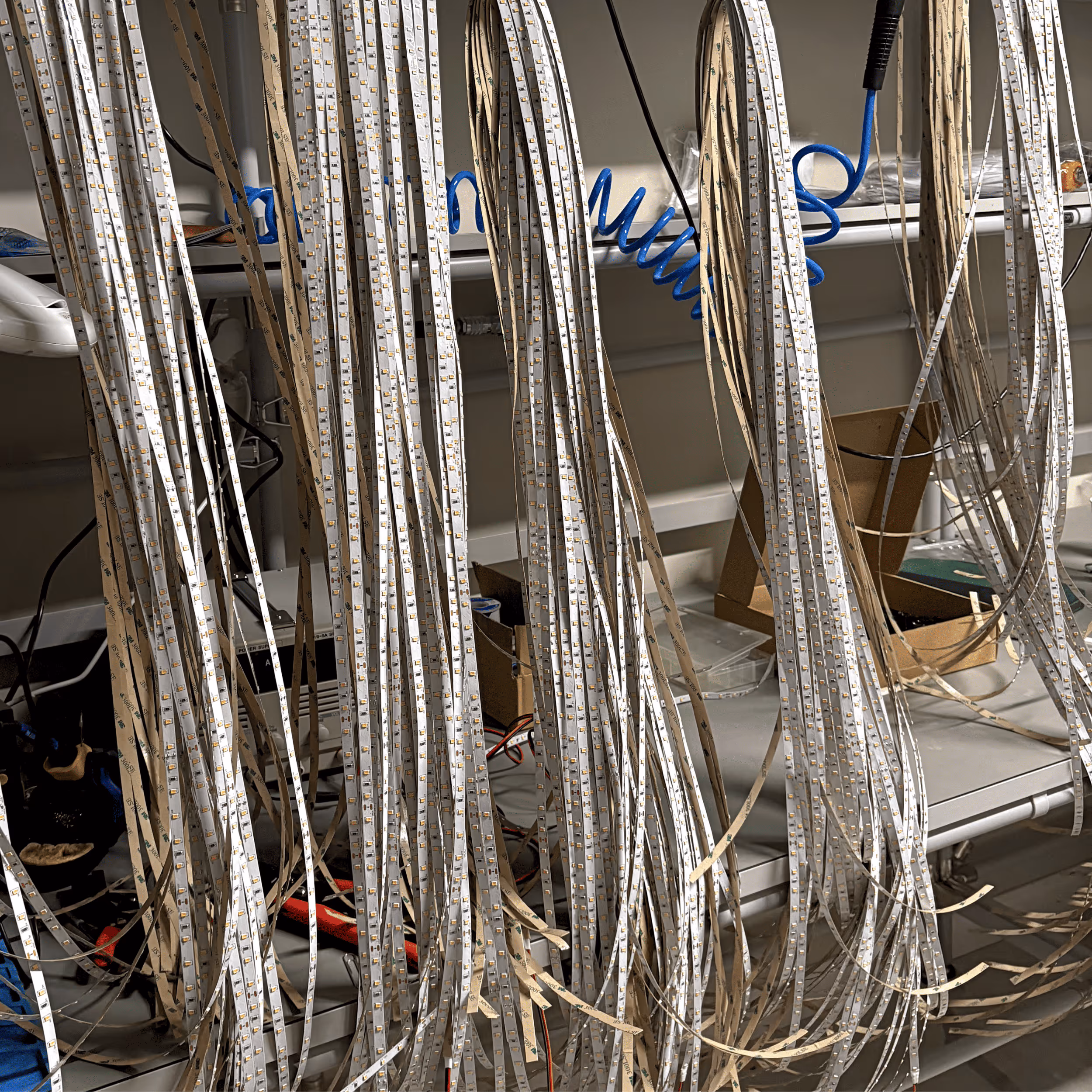 Long strips of LED lights hanging in front of metal shelves with tools and boxes behind.