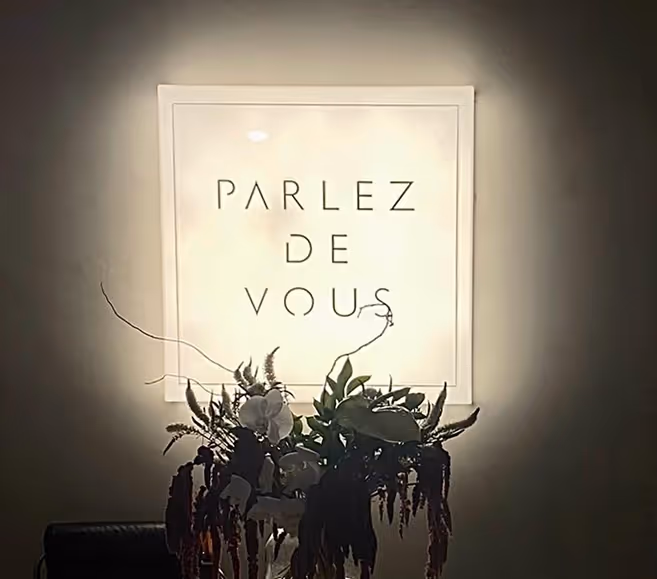 Illuminated framed sign with text 'PARLEZ DE VOUS' above a dark floral arrangement.