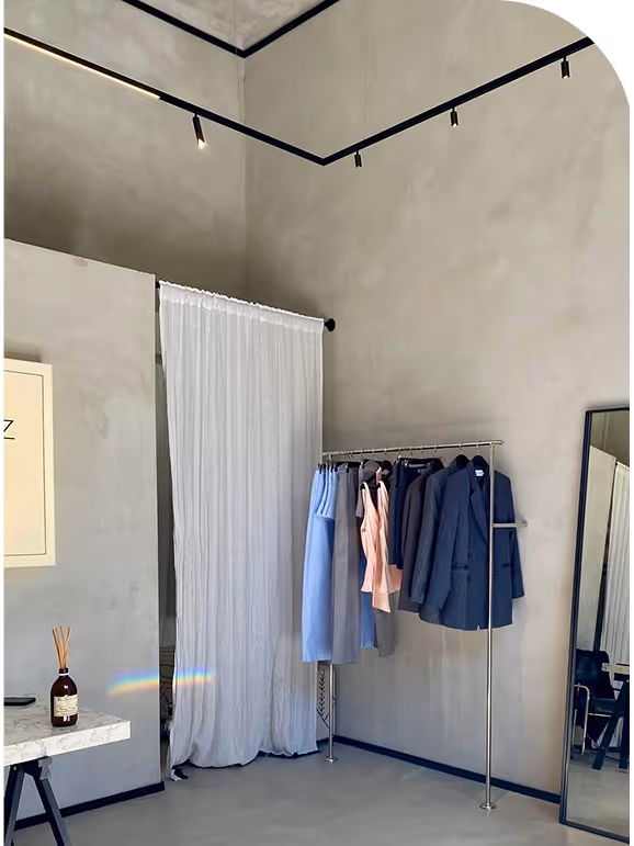 Minimalist room corner with gray walls, hanging clothes, a tall mirror, and a table with a reed diffuser.