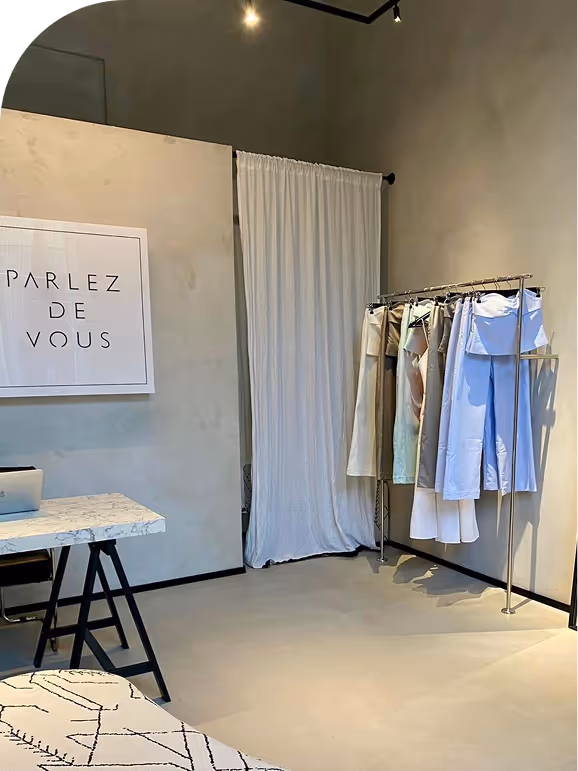 Minimalist room corner with clothes rack, light-colored clothes, marble desk, and framed ‘PARLEZ DE VOUS’ print.